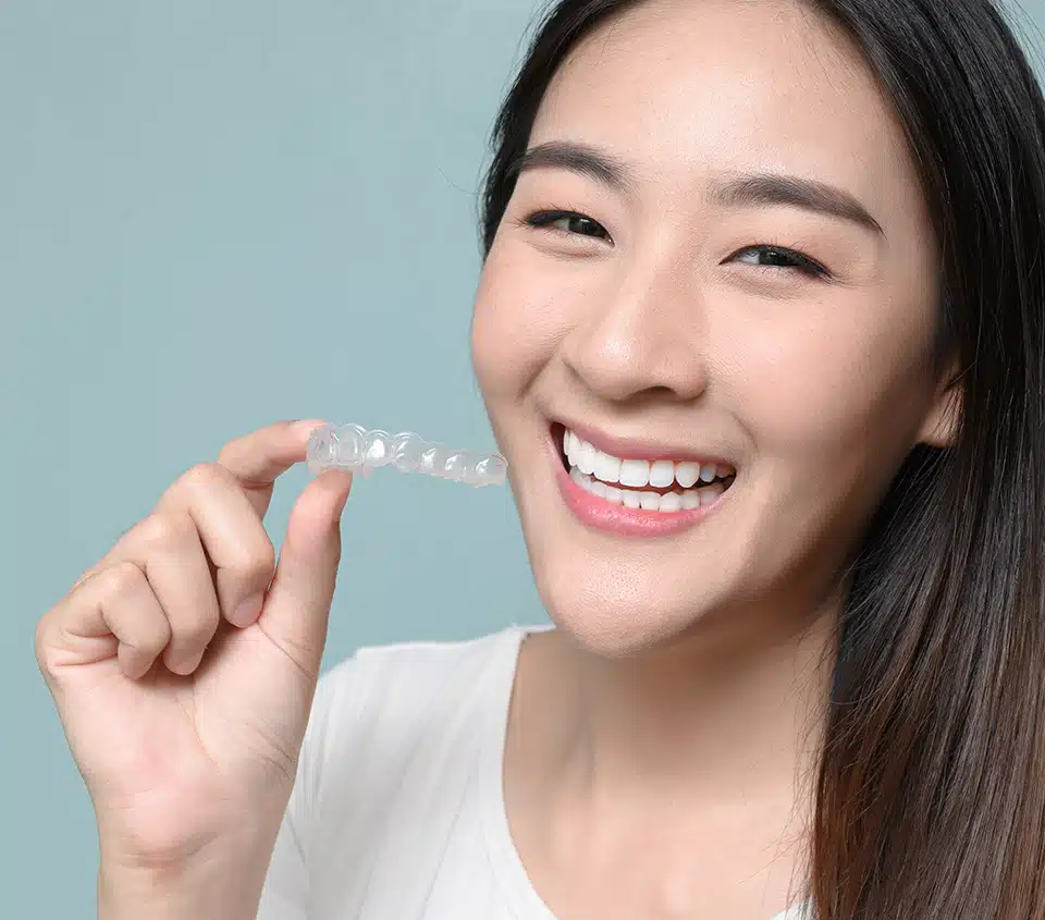 Smiling woman holding an Invisalign aligner in her hand while showing her teeth.